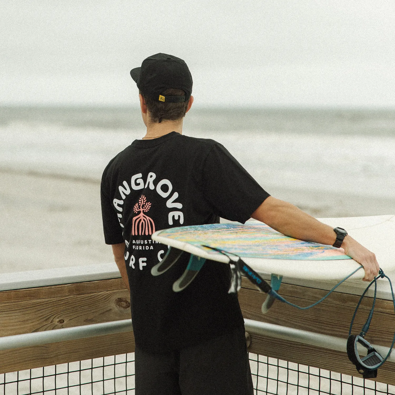 Surfer carrying a board in a Mangrove shirt